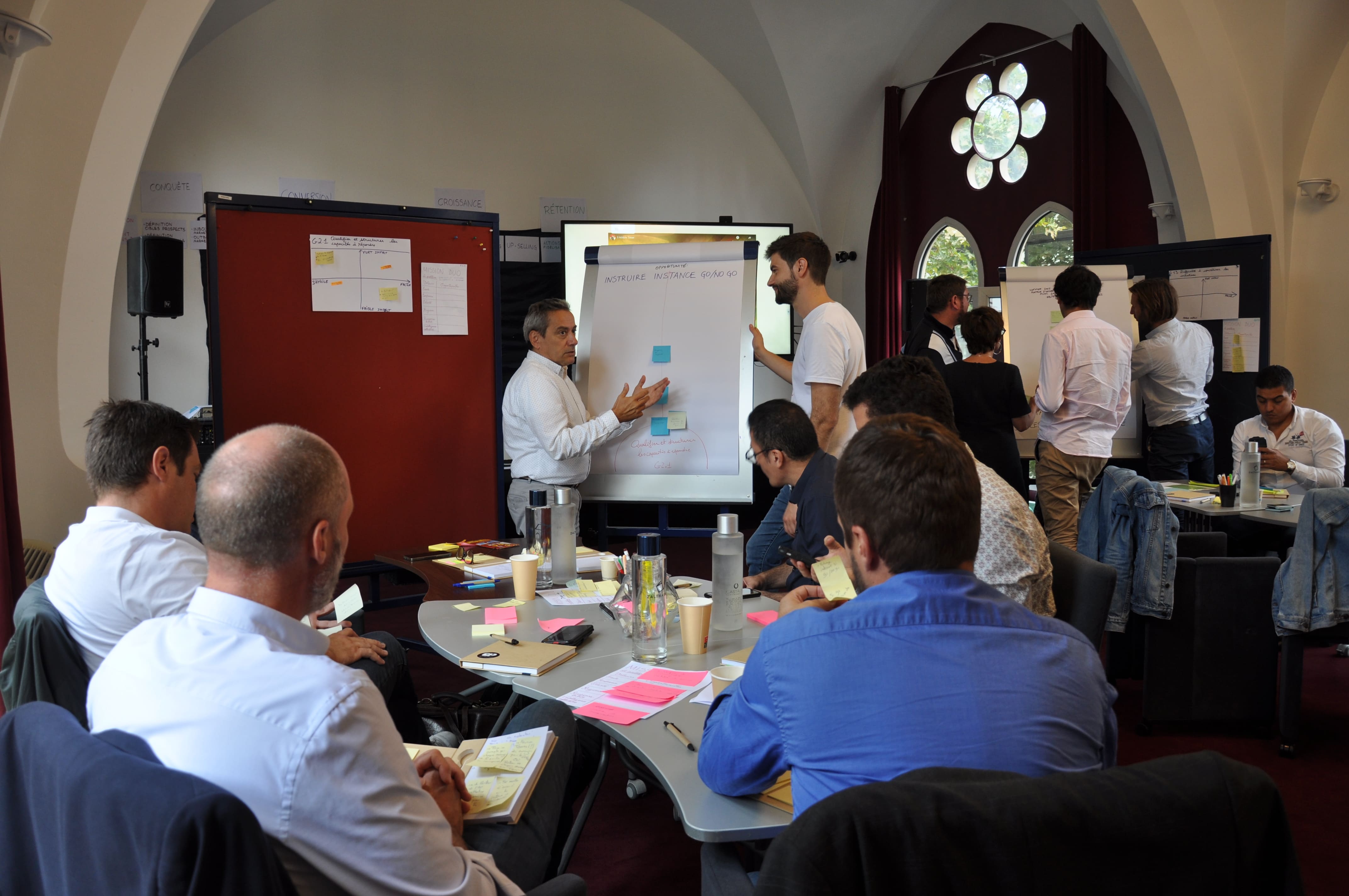 Vue large de la salle du séminaire avec ses voûtes d'arches, plusieurs groupes en travail simultané autour des paperboards.