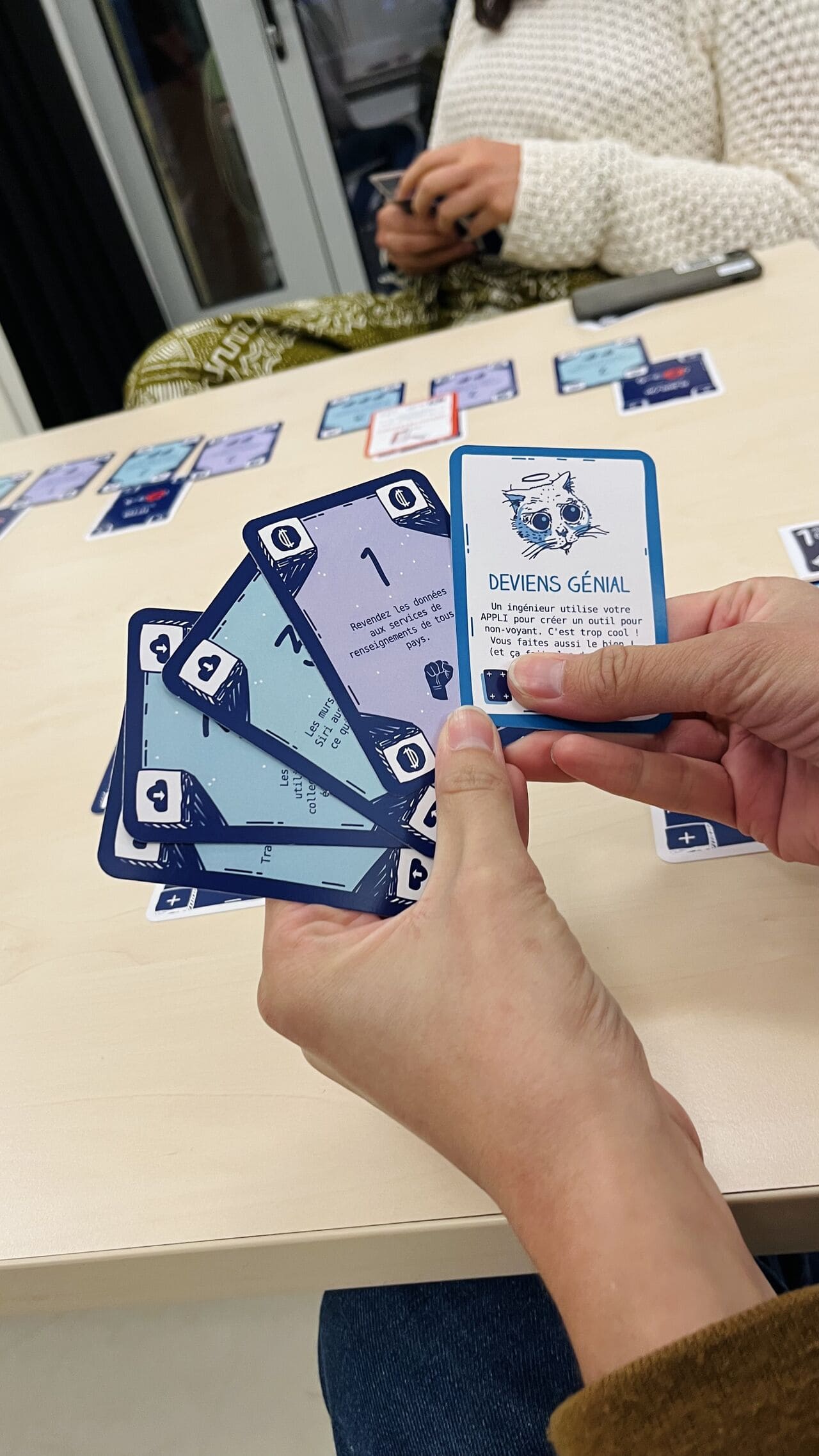 Détail des cartes Million Data Baby tenues en main, dont une carte « Deviens génial »